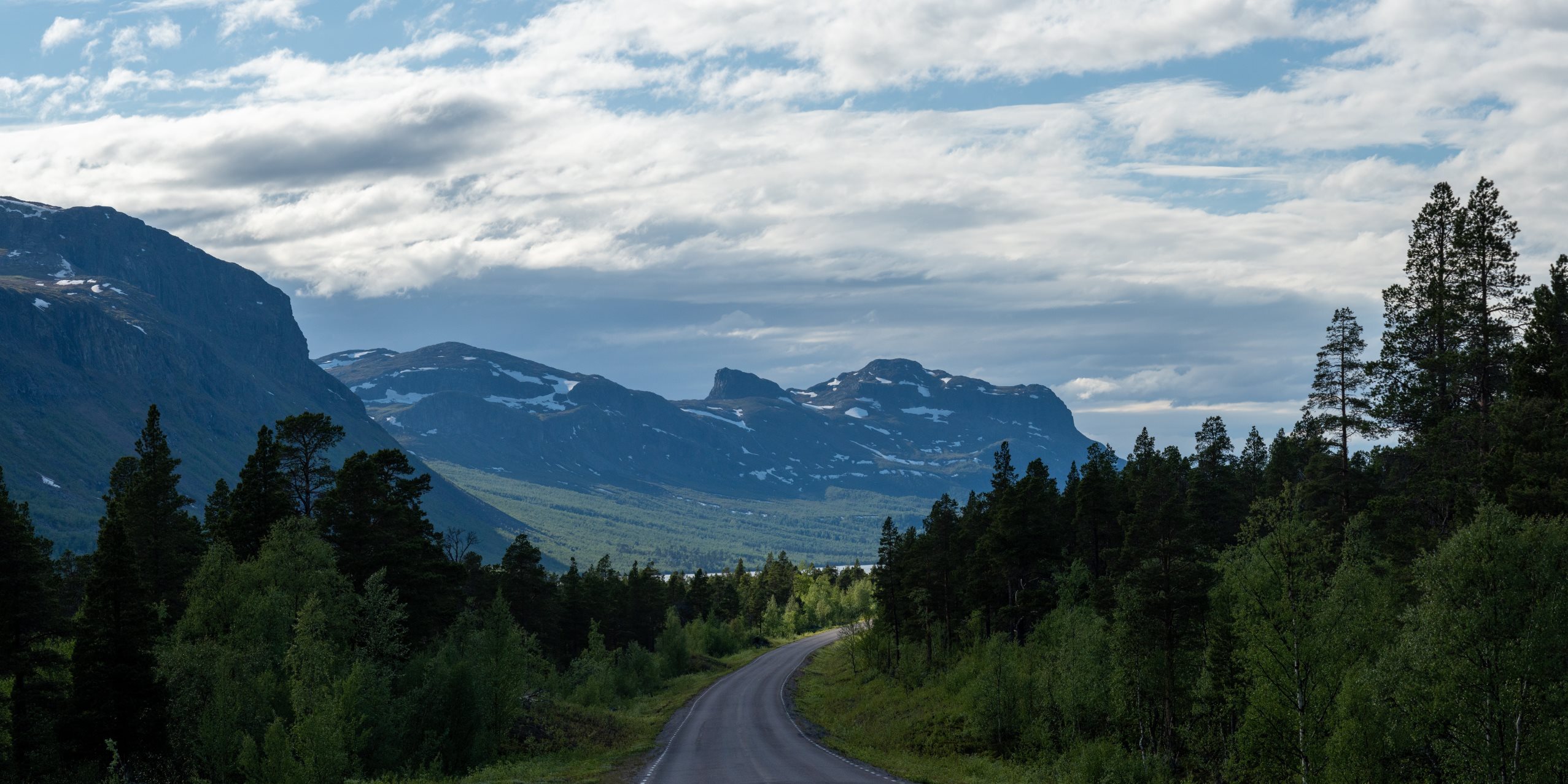 En väg i Gällivare kantad av skog och med berg i bakgrunden.