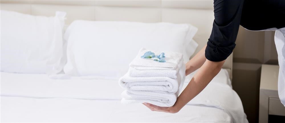 Hotellpersonal lägger fram vita vikta handdukar på en säng