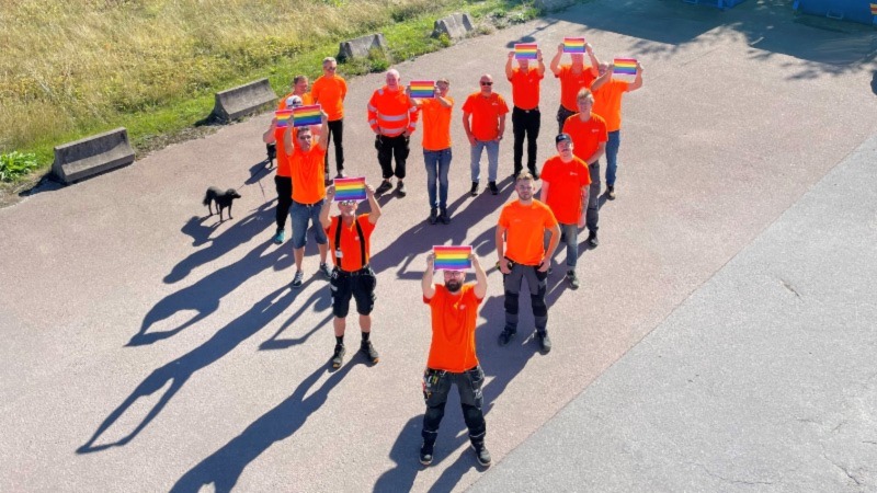 CERTEGO employees in orange shits standing in a heart formation holding pride flags